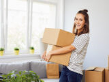 Junge Frau zieht in eine neue Wohnung ein und hält Kartons mit Habseligkeiten