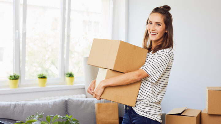 Junge Frau zieht in eine neue Wohnung ein und hält Kartons mit Habseligkeiten